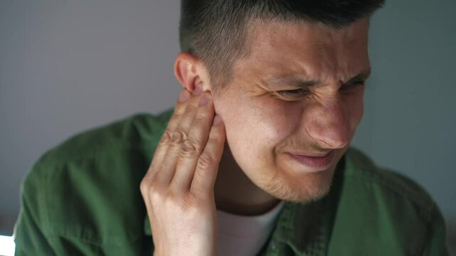 a young man in a green shirt has ear pain