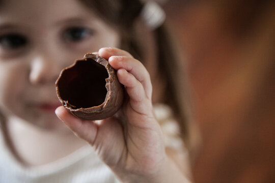 Child holding up hollow chocolate Easter egg she is eating
