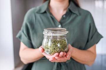 Close-up of peeled pumpkin seeds in a glass jar in a woman's hands emphasizes their benefits for the heart and blood vessels due to omega-3 fatty acids concept diet, medical institutions
