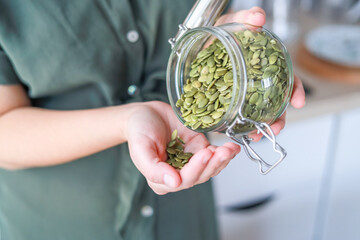 Woman pouring pumpkin seeds from a glass jar they support overall health due to their nutritional...