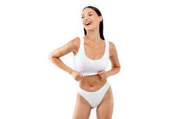 Fototapeta premium Excited young woman in white underwear top bra and panties standing posing over white background and smiling, showing her body figure