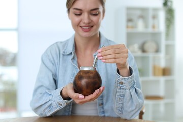 Woman with traditional yerba mate tea at table indoors, selective focus