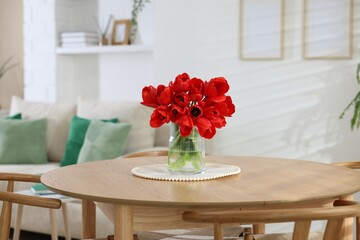 Beautiful red tulips in vase on wooden table indoors