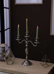 Elegant candlestick with burning candles and decor on table near brown wall