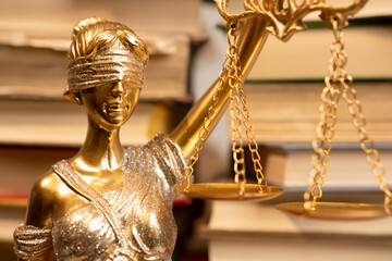Golden statue of Lady Justice holding scales positioned against a backdrop of stacked law books in...