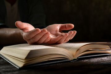 Hands reaching towards an open book in a dimly lit environment conveying a moment of reflection and contemplation