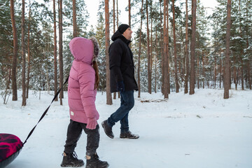 Dad with his daughter walking with snow tubing in the winter forest