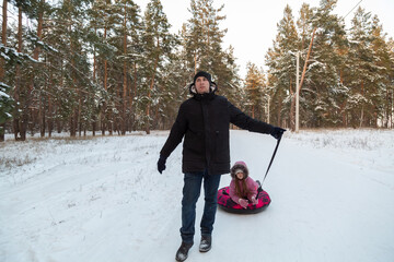 Father and daughter having fun with snow tube in the forest