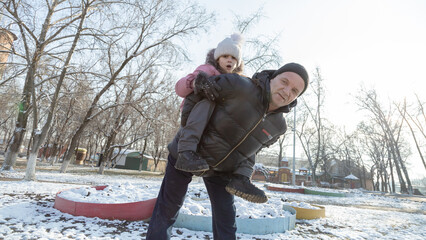 Grandfather playing with her granddaughter on the playground in the park in winter
