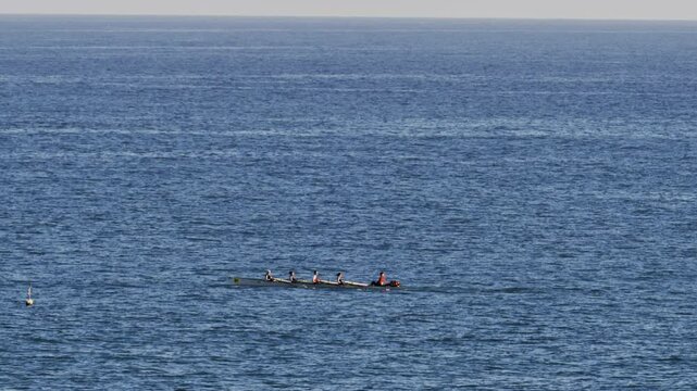 Distant view of a rowing team of four people practicing on calm water, with a coxswain seated at the front