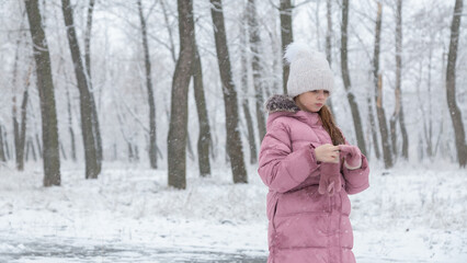 Child walking in the snow park enjoys the first snow in winter