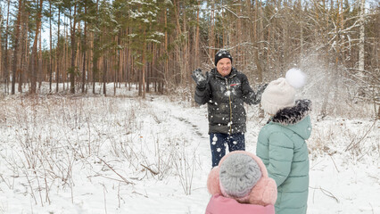 Little girls play with snow with her grandfather in winter forest
