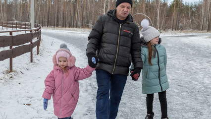 Little girls with her grandfather walking in park on snowy winter day