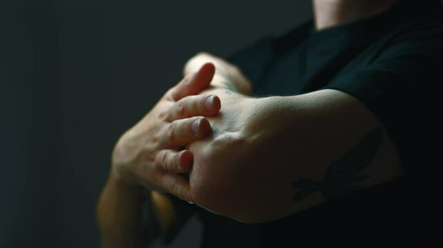 arm pain close up. 
A man suffers from severe pain in his arm.
A guy in black clothes with a sore arm.
Dark background in the room.
An adult man with a sore elbow
