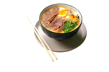 Black bowl with ramen, sliced meat, boiled eggs, greens, sprouts, and chopsticks on a white background. Cropped PNG object.