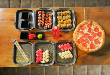 Sushi and pepperoni pizza on a table: fried rolls, rice rolls, wasabi, ginger — a fusion of Japanese and Italian cuisine.