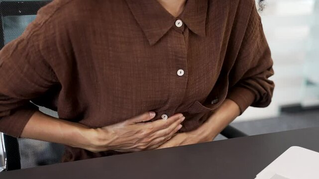 Close up. Female hands holding massaging stomach. Businesswoman feels stomach pain while sitting at workplace in business office. Sick woman suffers from gastritis, menstruation, poisoning or bloating