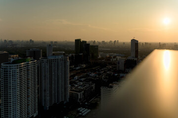 City skyline at sunset with glowing sunlight reflecting on a rooftop edge, creating a dramatic golden hour atmosphere over high-rise buildings and urban landscape