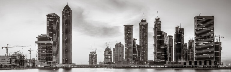 Fototapeta premium Monochrome city skyline with tall skyscrapers reflecting on calm water under a cloudy sky, Dubai Marina bay UAE