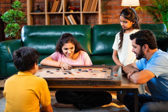Parents and children playing carrom board game indoors, laughing and aiming striker with focus