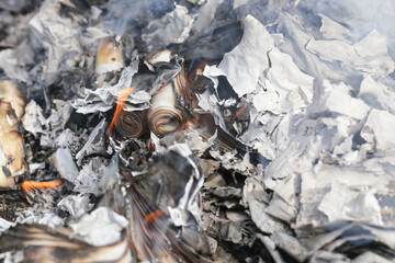 Burnt paper remains closeup texture. Charred curled pages in white ash and smoke background. Burned documents and fragile layers after fire. Hot glowing remnants. Destruction after combustion.