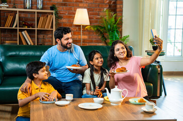 Indian family posing for selfie while enjoying samosa and tea time in warm and happy atmosphere