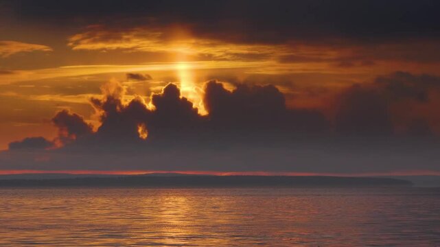 Sunset over Lake Imandra on Kola Peninsula with dramatic orange and red colors in the sky, clouds catching sunlight, and calm reflective water.