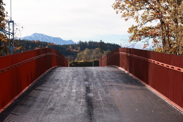 A bridge with a red railing and a view of the mountains