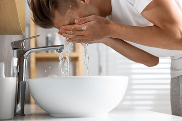 Man washing his face over sink in bathroom