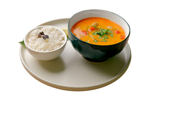 Green bowl with Tom Yum soup, parsley, and a small bowl of rice with lemon slices on a white plate. Cropped PNG object.