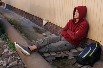 Homeless man sitting near yellow wall on city street