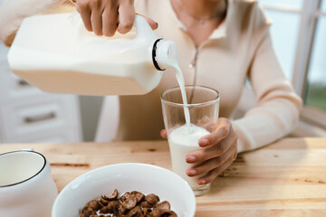 A woman prepares a healthy breakfast in her kitchen, pouring fresh milk into a bowl of muesli with blueberries—nutritious and homemade.