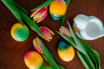 Easter table setting viewed from above, featuring colorful eggs, fresh spring flowers, and decorative chicks. A cheerful flatlay capturing the festive spirit of a joyful holiday celebration.
