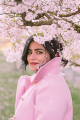 Portrait of a woman in pink coat under cherry blossoms in spring