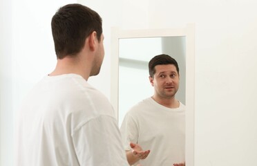Handsome man looking at himself in mirror indoors