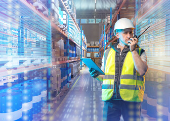 Warehouse worker in safety gear uses walkie-talkie and tablet for inventory control among stacked barrels and boxes in smart logistics environment. – Warehouse, Logistics.