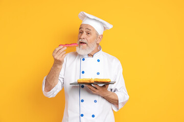 Professional pastry chef eating delicious eclair on orange background