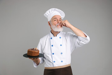 Professional pastry chef with delicious chocolate cake on grey background