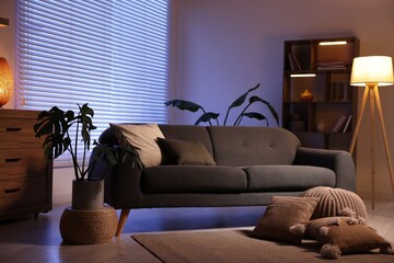 Stylish living room with comfortable sofa and wooden shelving unit in evening. Interior design