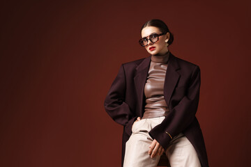Obraz premium Young woman in stylish clothes on chair against brown background, space for text