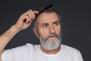 Fototapeta premium Handsome man combing his hair on dark grey background