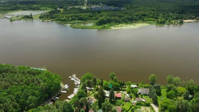Aerial footage showcases numerous leisure boats moored at a jetty in Jachranka, Serock, on Poland's Narew River. This local yacht club or marina is surrounded by summer homes and forest.