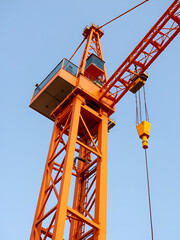 Tall orange construction crane with counterweight and cab, showcasing steel structure and lifting capabilities.