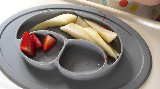 Baby taking a piece of strawberry with his dirty small hand, baby led weaning method