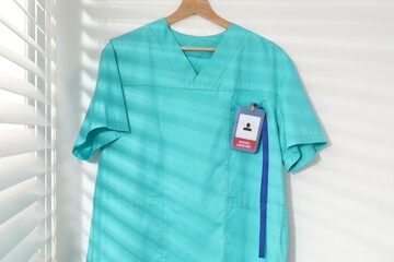 Medical worker uniform with badge on hanger against white wall