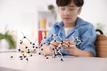 Boy making DNA structure model at desk indoors, selective focus