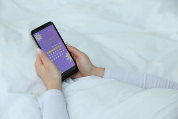 Menstruation. Woman using period calendar application on smartphone in bed indoors, closeup