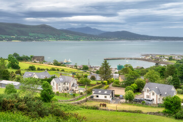 Experience the breathtaking Irish coastline, where colorful homes blend with a charming harbor amid vibrant green countryside stretching far and wide, Carlingford, Ireland