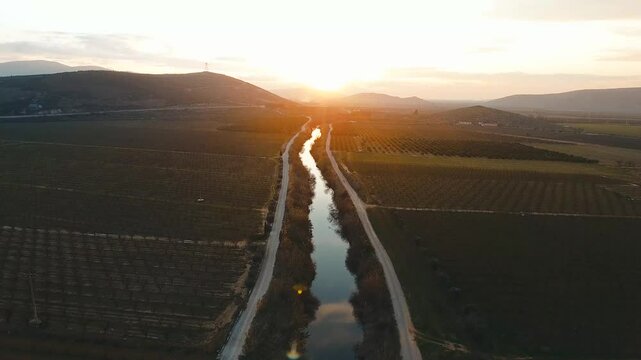 River flowing through fertile fields at sunset, 4K Cinematic Drone Shot, two scenes parallel to the ground and from above