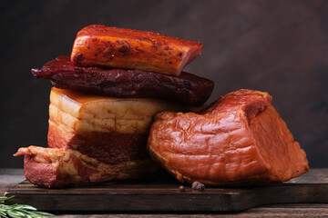 Close-up of various smoked and cured pork meats including brisket, loin, sausage, sliced and arranged on rustic wooden board.